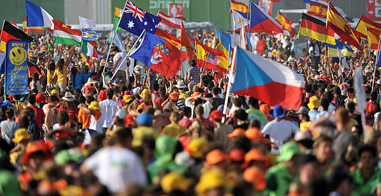 Menschenmenge bei Veranstaltung, viele bunte Fahnen verschiedener Länder, darunter Australien, Tschechien und Deutschland.