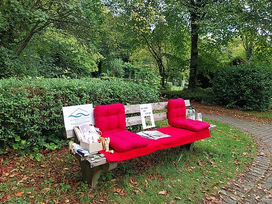 Parkbank mit roten Sitzkissen und Informationsmaterialien in einem grünen Park
