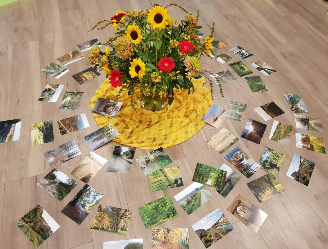Strauß aus Sonnenblumen und roten Blumen auf gelbem Tuch, umgeben von mehreren Fotos auf Holzboden.