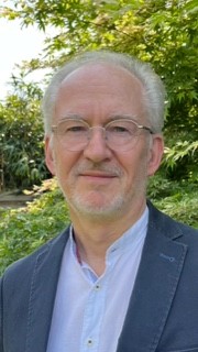 Wolfgang Soldin mit grauen Haaren trägt hellblaues Hemd und dunkelblauen Blazer, steht vor grünem Laub im Freien.